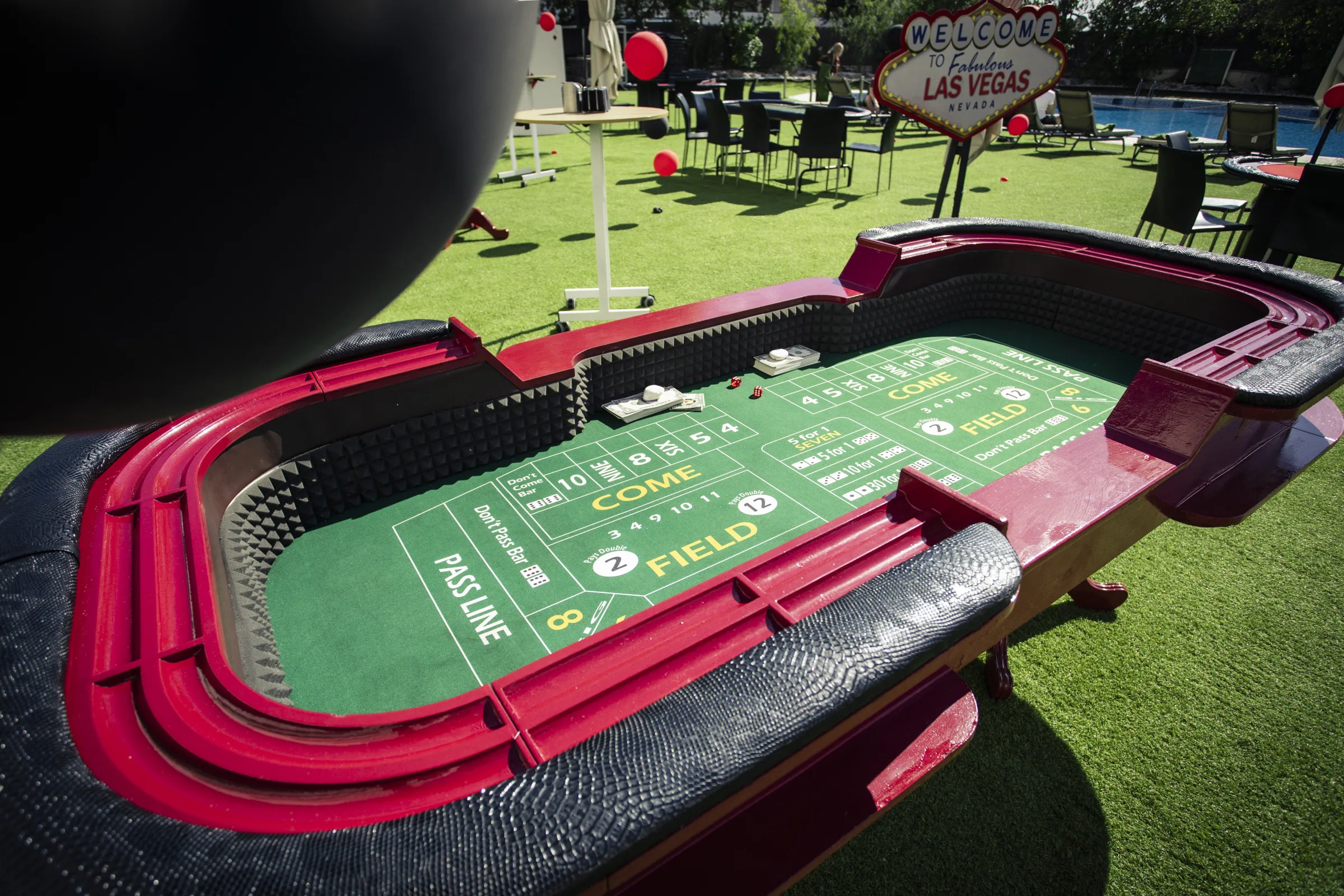 Casino gaming tables and a glowing Casino marquee on a lawn dotted with red and black balloons